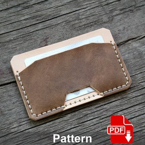 Può includere: Un porta carte in pelle marrone con cuciture bianche. Il porta carte ha una patta che si ripiega sulla parte superiore e una piccola tasca all'interno. Il porta carte è su una superficie di legno. Modello PDF.