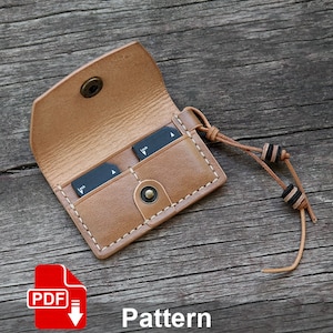 May include: A brown leather card holder with a strap and two slots for memory cards. The holder is on a wooden surface. Pattern.