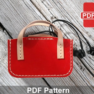 May include: A red leather earphone case with a beige handle and white stitching. The case is on a wooden surface with a pair of black earphones. The text "PDF Pattern" is at the bottom of the image.