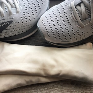 May include: A pair of gray running shoes with the word "BROOKS" on the side. The shoes are sitting on top of two white fabric shoe bags.