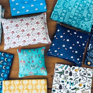 May include: Assortment of fabric squares with various patterns, including a blue square with white sailboats, a green square with white houses, a white square with blue moons, a yellow square with brown flowers, a blue square with white stars, a white square with green dinosaurs, a blue square with white moons, a green square with a red dragon, and a white square with red umbrellas.