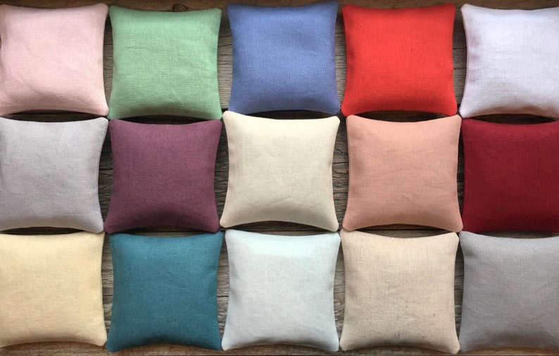 May include: A collection of 12 square-shaped pillows in various colors, including light pink, green, blue, red, beige, and gray. The pillows are made of a soft, textured fabric and are arranged in a grid pattern.