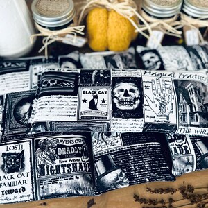 May include: Four black and white patterned fabric heat packs with various spooky Halloween designs, including a skull, a black cat, a hand with a palmistry chart, and a haunted house. The text on the fabric reads "Magical Practices", "Black Cat Coffee Company", "Raven's Cry Deadly Tonic", and "Lost! Black Cat Familiar Reward".