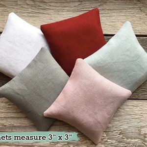 May include: Five fabric sachets in different colors, including white, red, gray, light blue, and pink. The sachets measure 3 inches by 3 inches. "sachets measure 3" x 3"