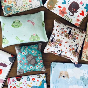 May include: Assortment of small, square and rectangular pillows with various animal and floral patterns. The pillows are made of soft fabric and have a variety of colors, including blue, green, pink, and brown.