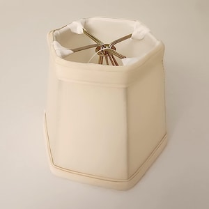 May include: A cream-colored, hexagonal lampshade with a gold metal frame.