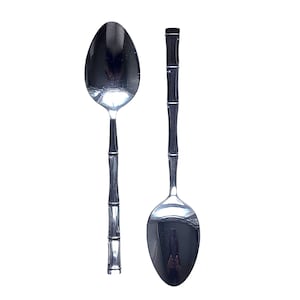May include: Two silver-toned metal spoons with a polished finish. Each spoon features a handle designed to resemble a stalk of bamboo with distinct segmented nodes. The bowls of the spoons are smooth, oval-shaped, and reflective, showing a metallic sheen.
