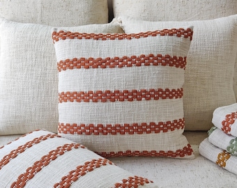 May include: A set of four throw pillows with a white background and orange stripes. The pillows are arranged on a white bedspread.