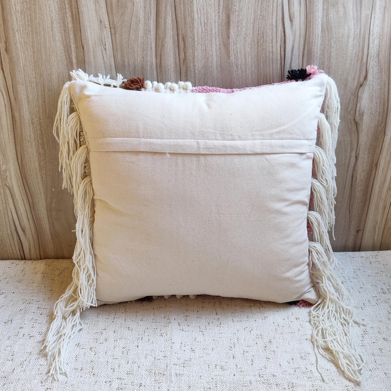 May include: A white throw pillow with a pink, white, and brown woven design and fringe trim. The pillow is shown from the back.
