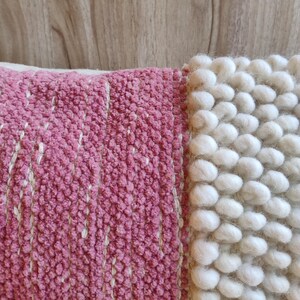 May include: A pink and white throw pillow with a textured woven design. The pillow has a pink side with a woven pattern and a white side with a fluffy, textured design.