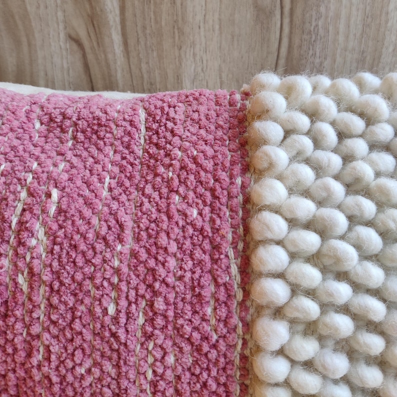 May include: A pink and white throw pillow with a textured woven design. The pillow has a pink side with a woven pattern and a white side with a fluffy, textured design.