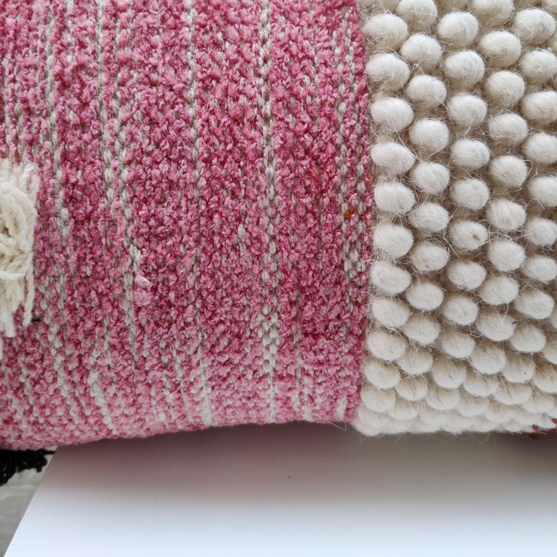 May include: A pink and white striped throw pillow with a textured surface. The pillow has a white pom-pom trim on one side.