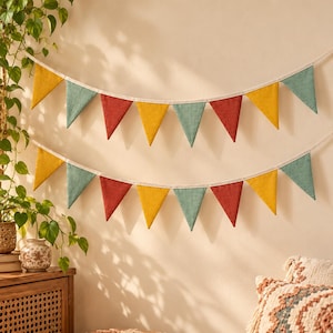 May include: Two rows of fabric bunting flags suspended on a white string. The triangular pennants feature a repeating pattern of mustard yellow, muted teal, and terracotta red colors, creating a decorative banner display.