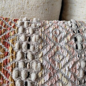 May include: Close-up of a beige and cream textured fabric with a woven pattern. The fabric has a subtle pink and yellow colour variation.