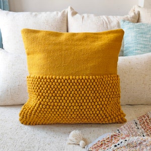 May include: A mustard yellow throw pillow with a textured, bumpy bottom half. The pillow is on a white sofa with other cushions.