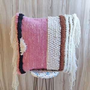 May include: A pink and white throw pillow with a fringe border. The pillow has a textured design and is made of woven fabric.