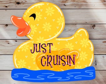 Może przedstawiać: Żółta gumowa kaczka z kwiatowym wzorem i napisem "JUST CRUISIN'" na niej. Kaczka pływa w niebieskiej wodzie.