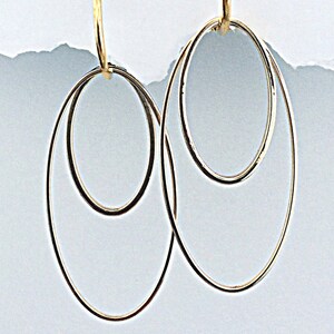 May include: A pair of gold hoop earrings with a double circle design. The earrings are made of a thin, delicate metal and have a simple, elegant style.