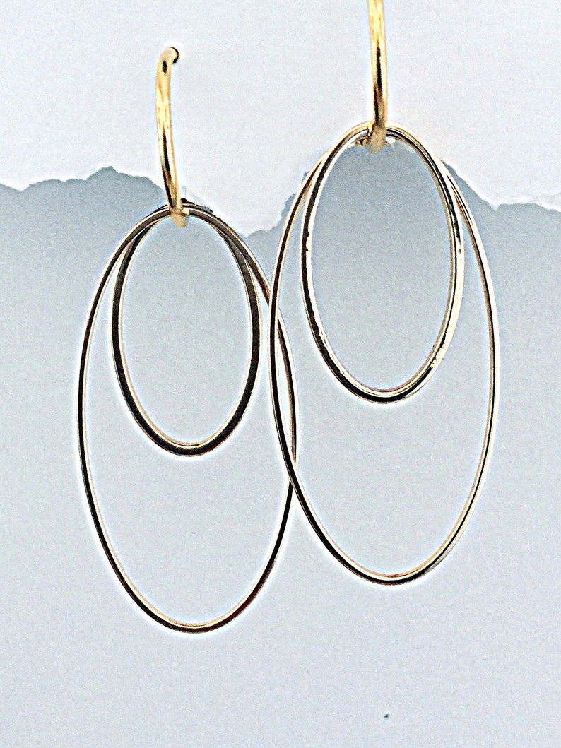 May include: A pair of gold hoop earrings with a double circle design. The earrings are made of a thin, delicate metal and have a simple, elegant style.