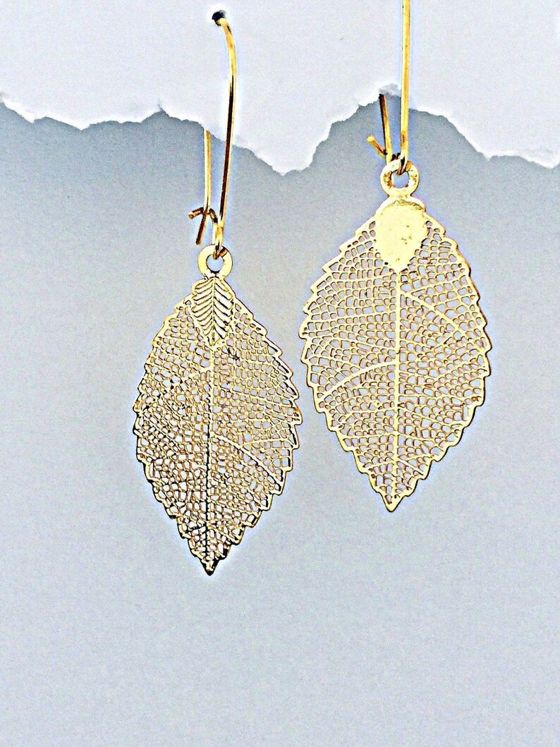 May include: A pair of gold leaf-shaped earrings with delicate filigree details. The earrings are suspended from thin gold hoops.