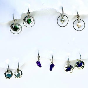 May include: Assortment of silver hoop earrings with various gemstone and pearl accents. The earrings feature a variety of styles, including simple hoops, double hoops, and hoops with a single gemstone or pearl hanging from the bottom.
