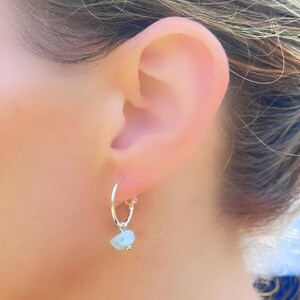May include: Silver hoop earrings with a light blue gemstone charm hanging from the bottom.