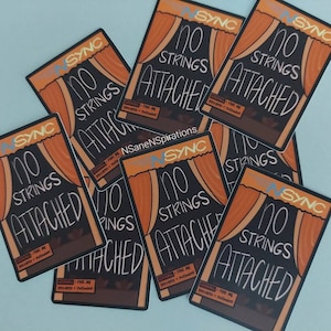 May include: Multiple stickers with the text "No Strings Attached" in black and white lettering on a black background. The stickers have a brown and orange curtain design with the text "NSync" in blue lettering.