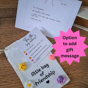 May include: A white fabric drawstring pouch labeled little bag of friendship with small resin charms including a yellow star, white daisy, purple balloons, and a rainbow. A card reads This little bag contains and a note says JUST A NOTE TO SAY...