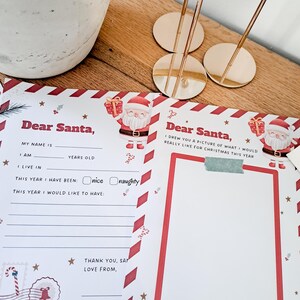 May include: A festive Christmas letter to Santa Claus, featuring a red and white border design with Santa Claus illustrations. The letter includes fill-in-the-blank sections for the child's name, age, and desired gifts. Gold-colored place card holders are in the background.