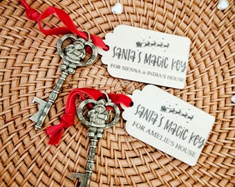 May include: Two decorative antique-style keys with red ribbons and attached tags that read "Santa's Magic Key" and personalized names. The keys are silver-colored and rest on a woven wicker basket, with heart-shaped embellishments.