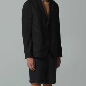 May include: A black blazer with a single button closure and a pocket on the left side. The blazer is worn over a pair of dark blue shorts.
