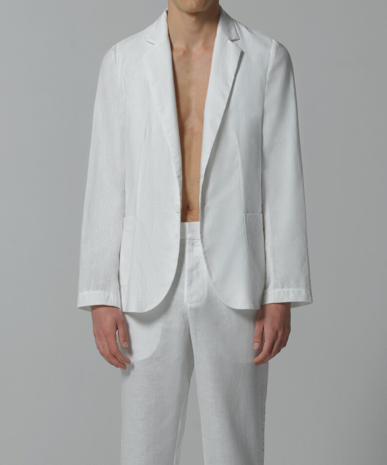 May include: A white linen blazer with a single button closure and a pocket on the left side. The blazer is unbuttoned and the person is wearing white linen pants.