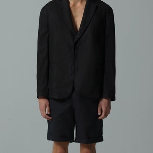 May include: A black linen blazer with a two-button closure and a relaxed fit. The blazer is paired with dark blue linen shorts.