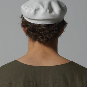 May include: A white cotton cap with a rounded crown and a flat brim. The cap is made of a soft, lightweight fabric and has a simple, classic design.