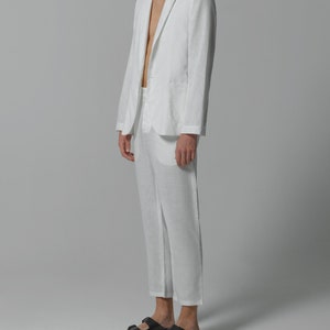 May include: A white linen suit with a blazer and matching pants. The blazer has a single button closure and a notched lapel. The pants are cropped and have a straight leg.