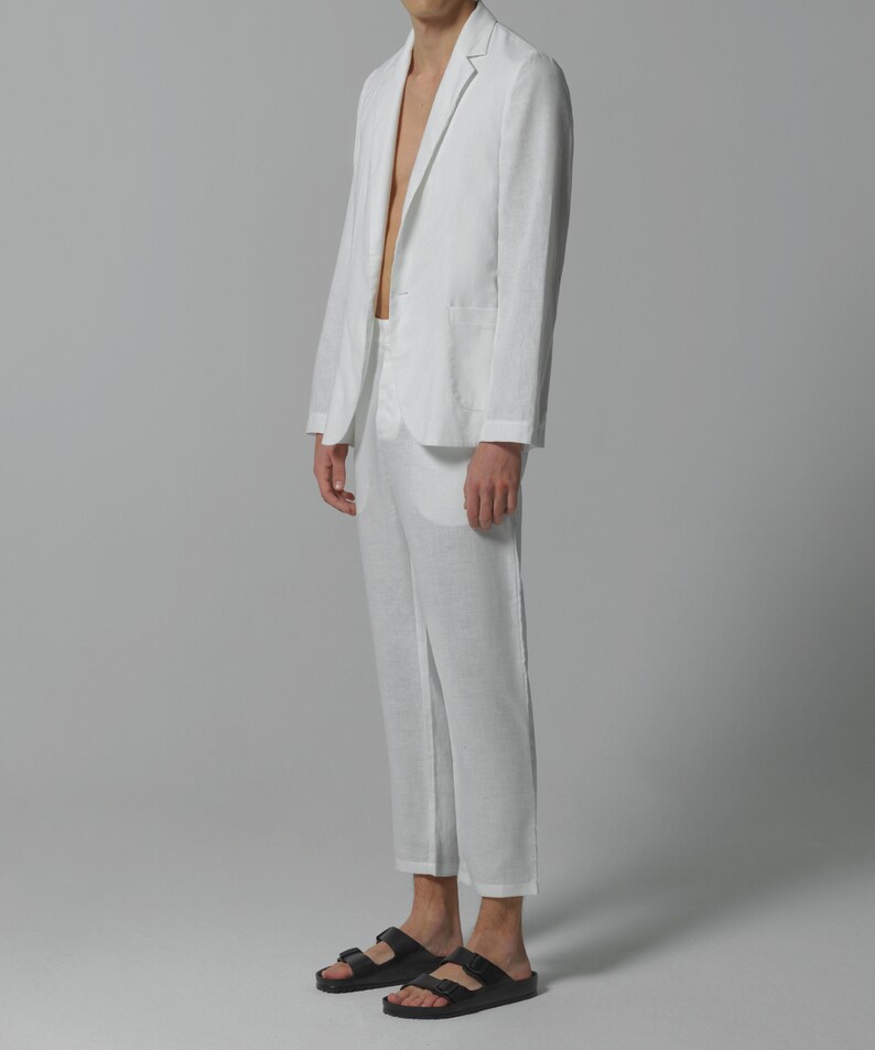 May include: A white linen suit with a blazer and matching pants. The blazer has a single button closure and a notched lapel. The pants are cropped and have a straight leg.
