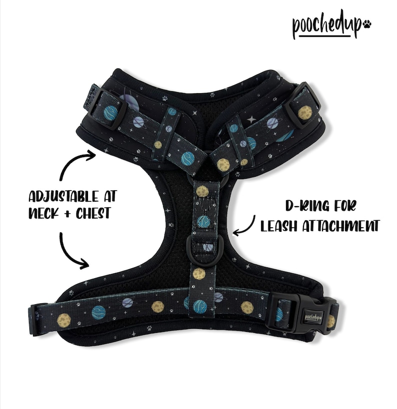 May include: A black dog harness with a space-themed print featuring planets and stars. The harness has adjustable straps at the neck and chest and a D-ring for leash attachment. The brand name "pooched up" is printed on the strap.