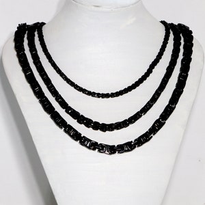 May include: Four black chain necklaces of varying lengths, layered on a white mannequin bust.