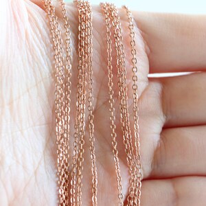 May include: Multiple strands of rose gold chain, arranged in a fan shape on a hand.