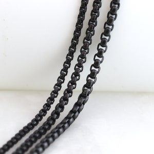May include: Three black chain necklaces of varying lengths and thicknesses. The chains are made of metal and have a matte finish.