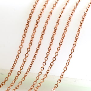 May include: Multiple strands of copper chain in various lengths, displayed on a white surface. The chains are made of small, linked circles.