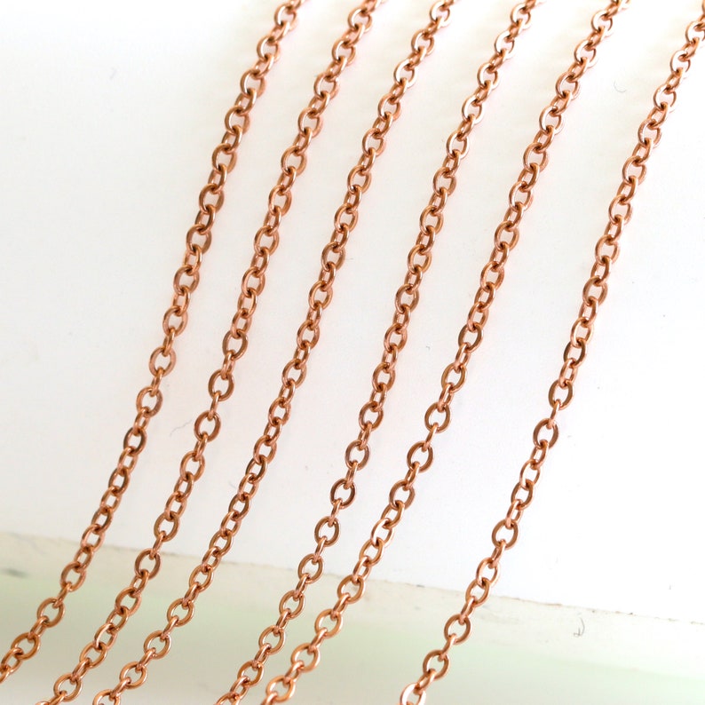 May include: Multiple strands of copper chain in various lengths, displayed on a white surface. The chains are made of small, linked circles.
