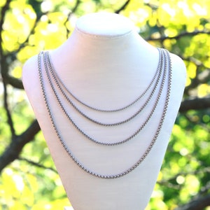 May include: Four silver chain necklaces of varying lengths displayed on a white mannequin bust against a blurred green background.