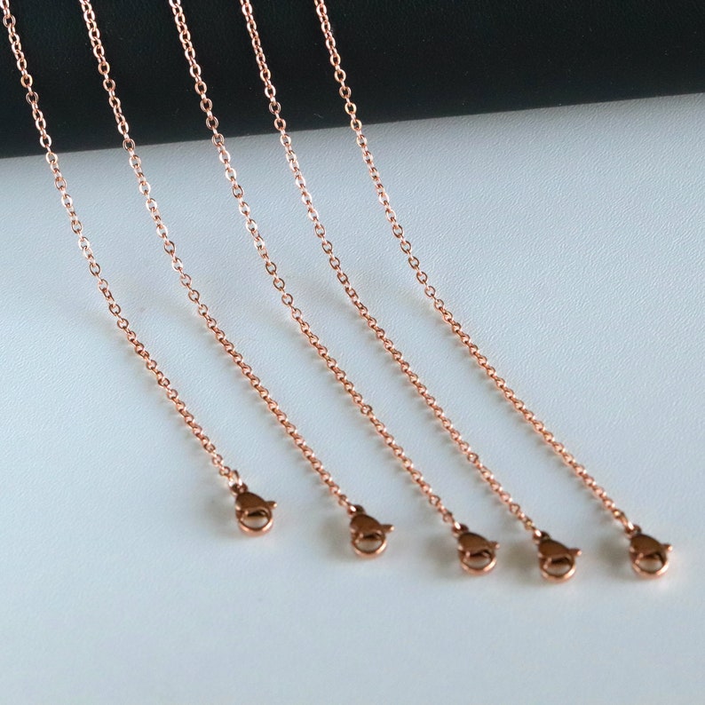 May include: Five rose gold chains with lobster claw clasps. The chains are arranged in a row, with the clasps facing the viewer.