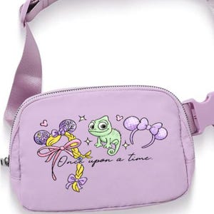 May include: A lavender fanny pack with a matching adjustable strap and buckle. The pack features a graphic of a green chameleon, a bow, and the text "Once upon a time." The design includes yellow, pink, and purple accents.