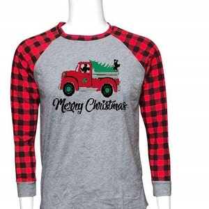 Op de afbeelding: Bijpassende kerstpyjamaset. De top is grijs met rode mouwen en een afbeelding van een rode vrachtwagen met een kerstboom. De tekst "Merry Christmas" staat eronder. De broek is rood en zwart geruit.