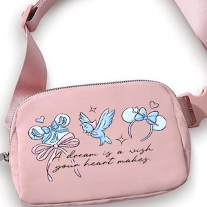 May include: A pink fanny pack with a matching adjustable strap and buckle. The pack features a whimsical design with illustrations of bows, a bird, and the text "A dream is a wish your heart makes."