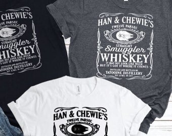 May include: Three t-shirts with a whiskey label design. The shirts are black, grey, and white. The label reads "Han & Chewie's Straight Smuggler Whiskey" with the text "It may not look like much but it's got it where it counts."