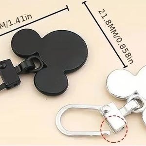 Op de afbeelding: Twee metalen ritsen met een Mickey Mouse-ontwerp. De rits aan de linkerkant is zwart en 3,57 cm lang. De rits aan de rechterkant is zilver en 2,18 cm lang.
