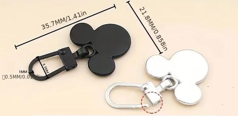 Op de afbeelding: Twee metalen ritsen met een Mickey Mouse-ontwerp. De rits aan de linkerkant is zwart en 3,57 cm lang. De rits aan de rechterkant is zilver en 2,18 cm lang.
